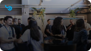 Pessoas conversando em um evento da Softfocus, usando camisetas e crachás da empresa. O ambiente é iluminado, com plantas ao fundo e um logotipo da Softfocus no canto superior esquerdo. 